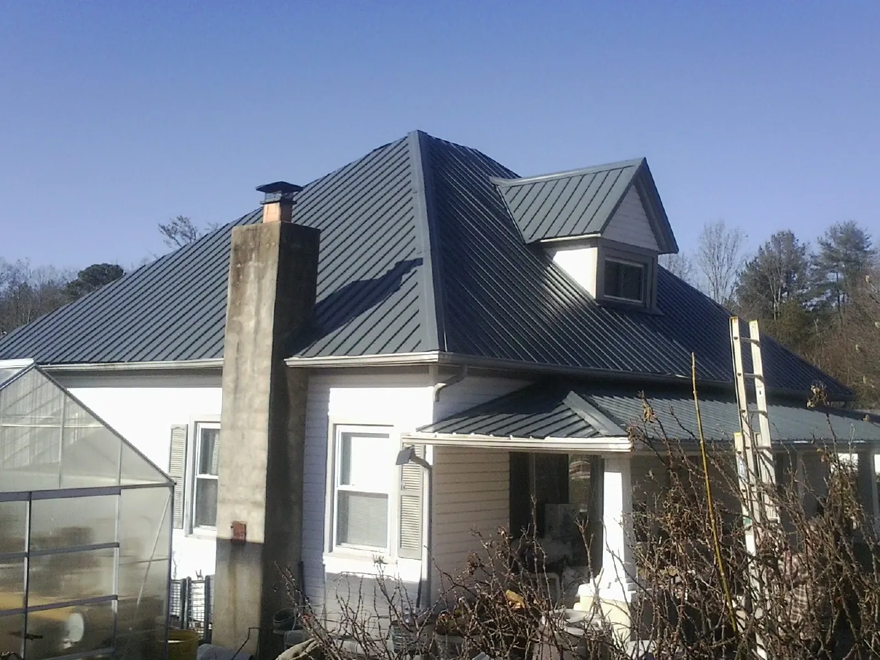 Dark blue standing seam metal roof on a white farmhouse with dormer — Slate & Tile Roof Repair by Roofing Brothers in Douglass