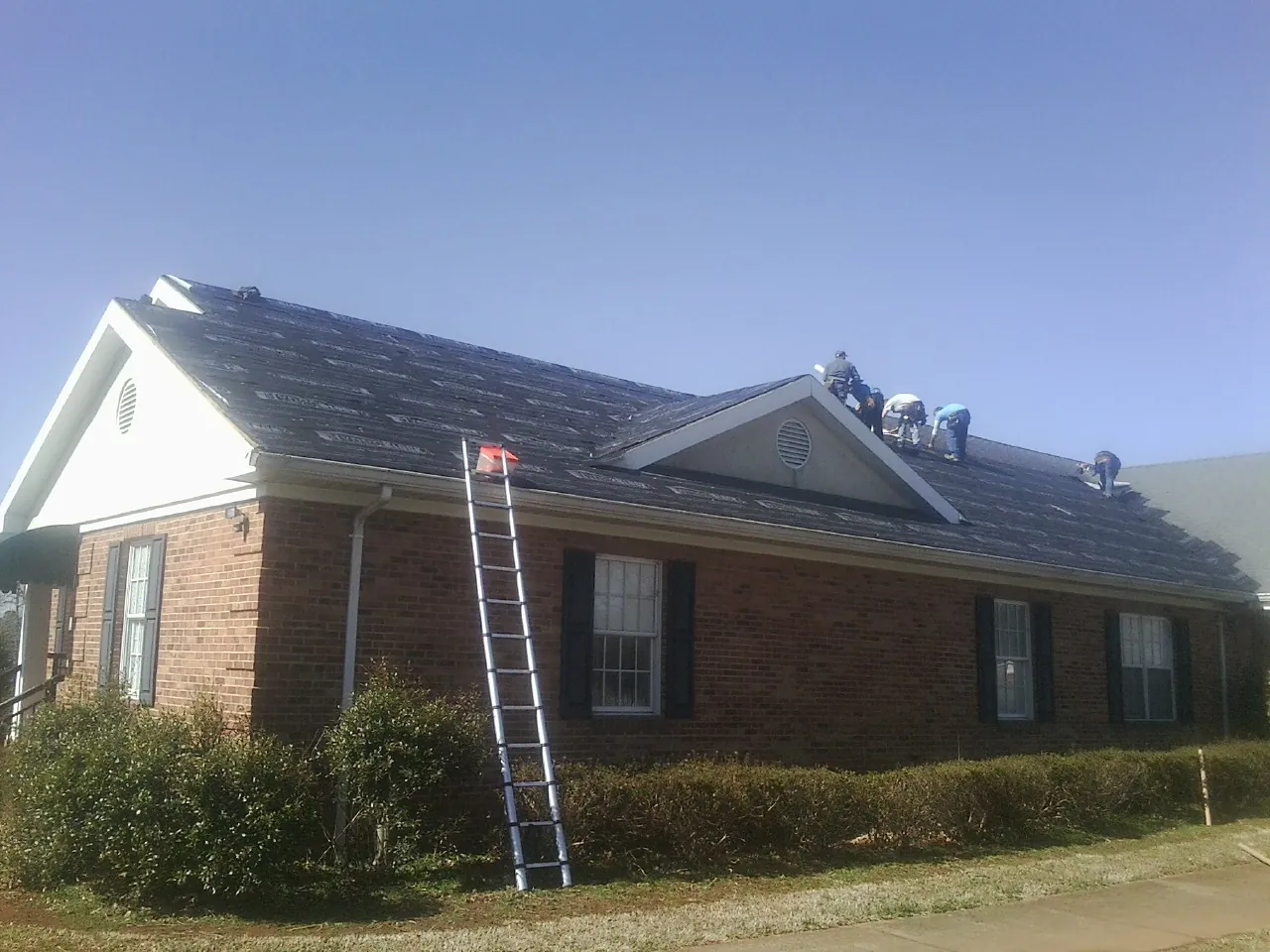 Crew tearing shingles off a brick ranch roof with a ladder set — Emergency Roof Repair work by our crew in Douglass