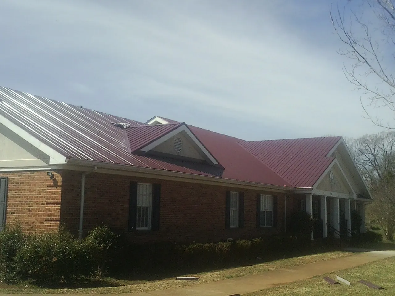 Red metal roof with gabled entries on a long brick building, from a Hail Damage Roof Repair job in Douglass