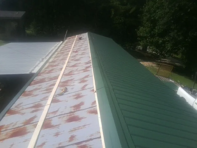 Old rusted panels beside newly installed green metal roofing — Wind Damage Roof Repair by Roofing Brothers in Douglass
