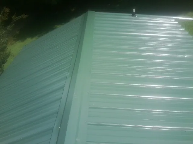 New green metal panels meeting at the ridge of a roof — Flat Roof Repair work by our crew in Douglass