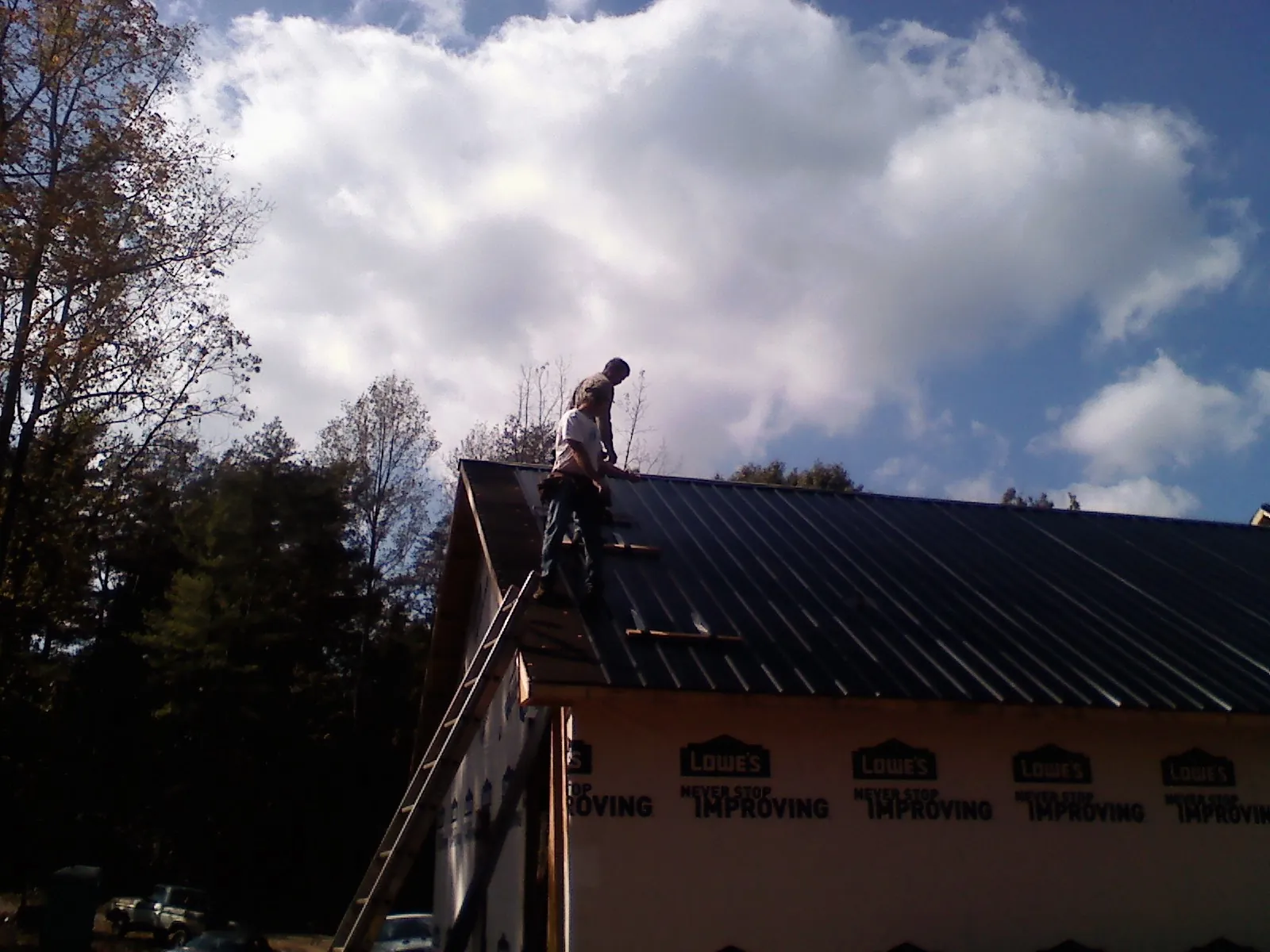 Roofer fastening dark metal panels high against a cloudy sky, from a Roof Inspection job in Douglass