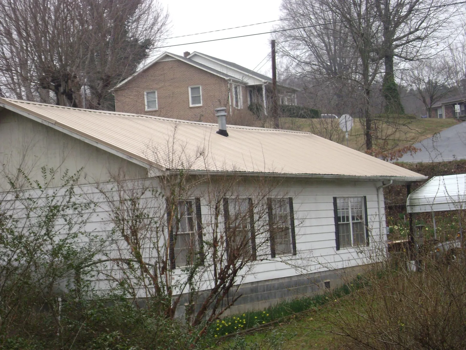 Tan metal roof on a white sided house set into a hillside — Commercial Roofing by Roofing Brothers in Douglass