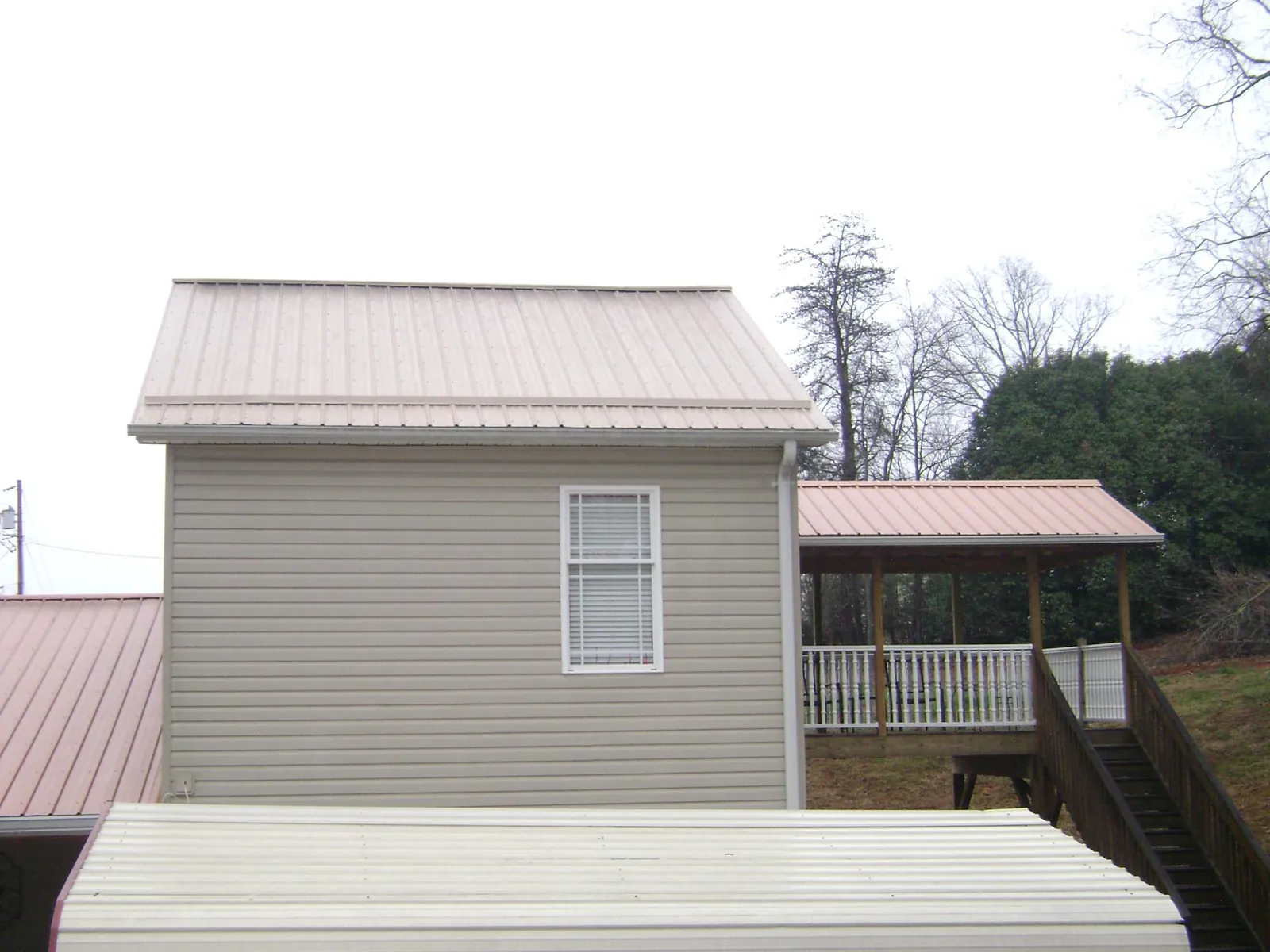 Tan metal roofs on a two story addition and attached porch, from a Roof Replacement job in Douglass