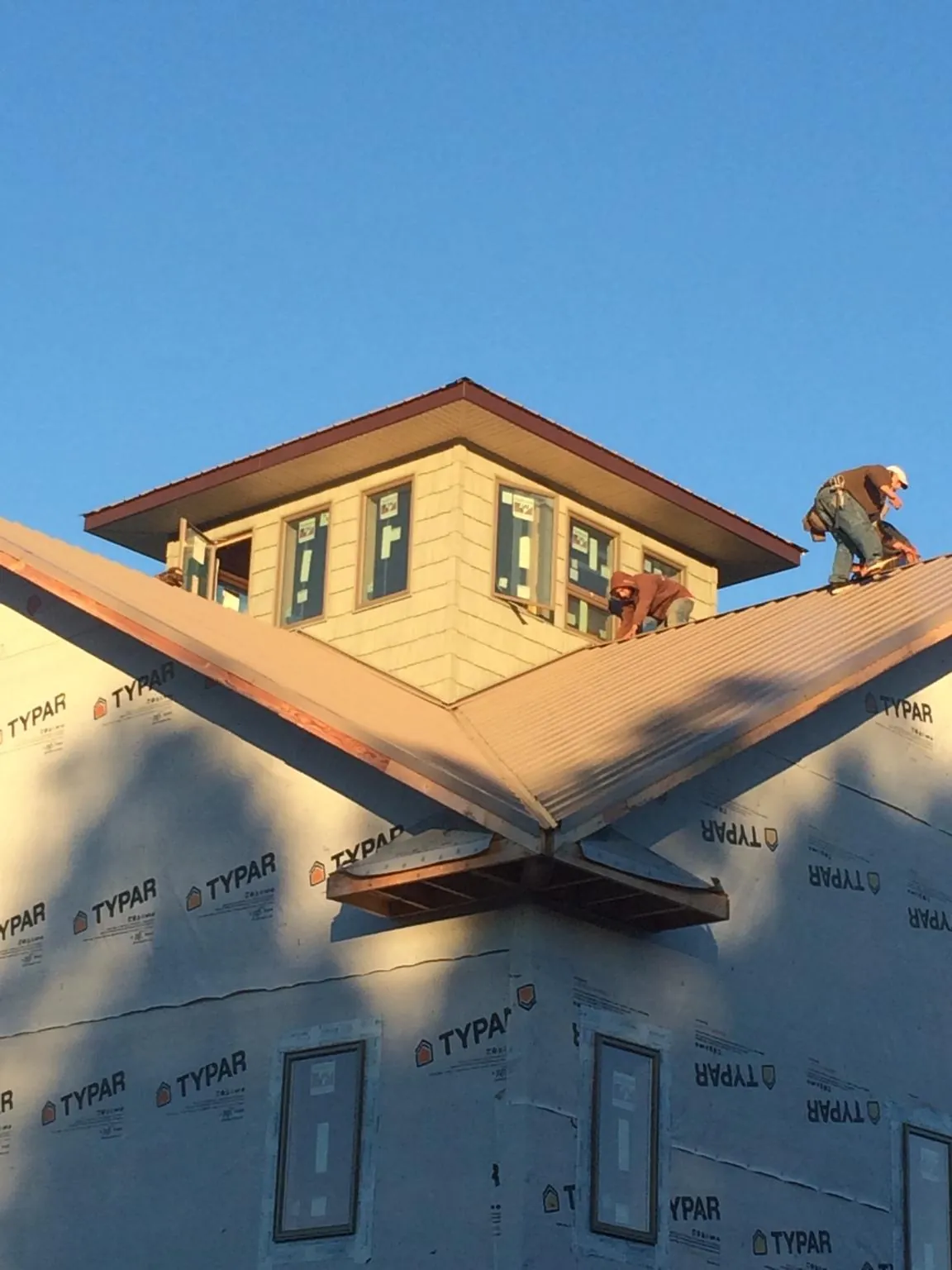 Roofers working around a rooftop cupola on a new metal roof at sunset — Roof Waterproofing in Douglass by Roofing Brothers